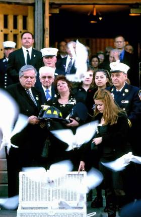 Doves were released at the funeral of Christopher Santora while his mother Maureen holds his helmet. Santora, who was a probie firefighter and the youngest in the house, had already signed out after completing his shift when he heard the bell sound and jumped on a truck heading to the WTC where he and 14 colleagues would perish.