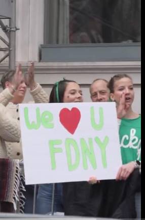 Spectators hold up a sign as firefighters proceed up Fifth Ave.